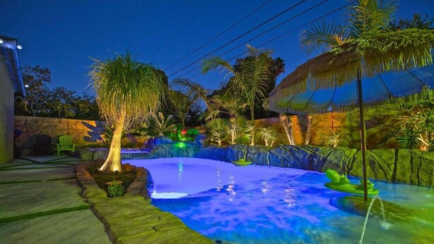 A swimming pool with a tropical theme, surrounded by palm trees and a stone wall.