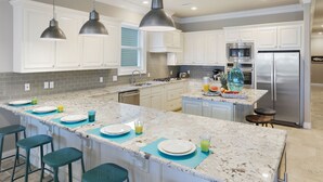 A modern kitchen with white cabinets, granite countertops, stainless steel appliances, and teal bar stools.