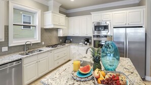 A kitchen with white cabinets, stainless steel appliances, a granite countertop, and a fruit basket.
