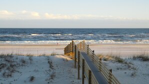 A wooden boardwalk leading to the beach with sand dunes and the ocean in the background.