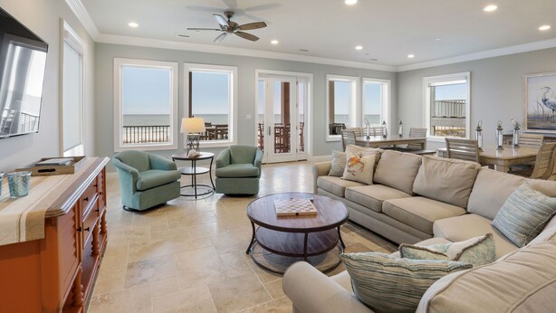 A spacious living room with a large sofa, armchairs, a coffee table, and a view of the ocean through large windows.