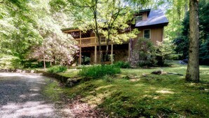 A rustic cabin with a wooden deck, surrounded by lush greenery and a stone pathway. - Private Creek, Hiking Trail System, Trout Fishing Onsite + Game Room, WiFi, Fire (Robbinsville)