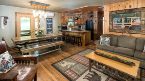 A cozy, rustic interior with wooden flooring, a bar area, and a seating area with a sofa and a bench. - Private Creek, Hiking Trail System, Trout Fishing Onsite + Game Room, WiFi, Fire (Robbinsville)