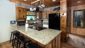 A kitchen with wooden cabinets, granite countertops, a black refrigerator, and hanging pots. - Private Creek, Hiking Trail System, Trout Fishing Onsite + Game Room, WiFi, Fire (Robbinsville)