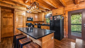 A wooden cabin kitchen with a central island, bar stools, a refrigerator, and a microwave.
