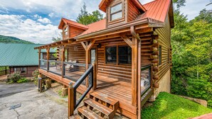 A log cabin with a balcony, a porch, and a small deck.