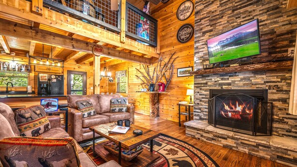 A cozy lodge interior with a fireplace, a television, and a dining area.