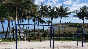 Una playa arenosa con palmeras y un parque infantil.