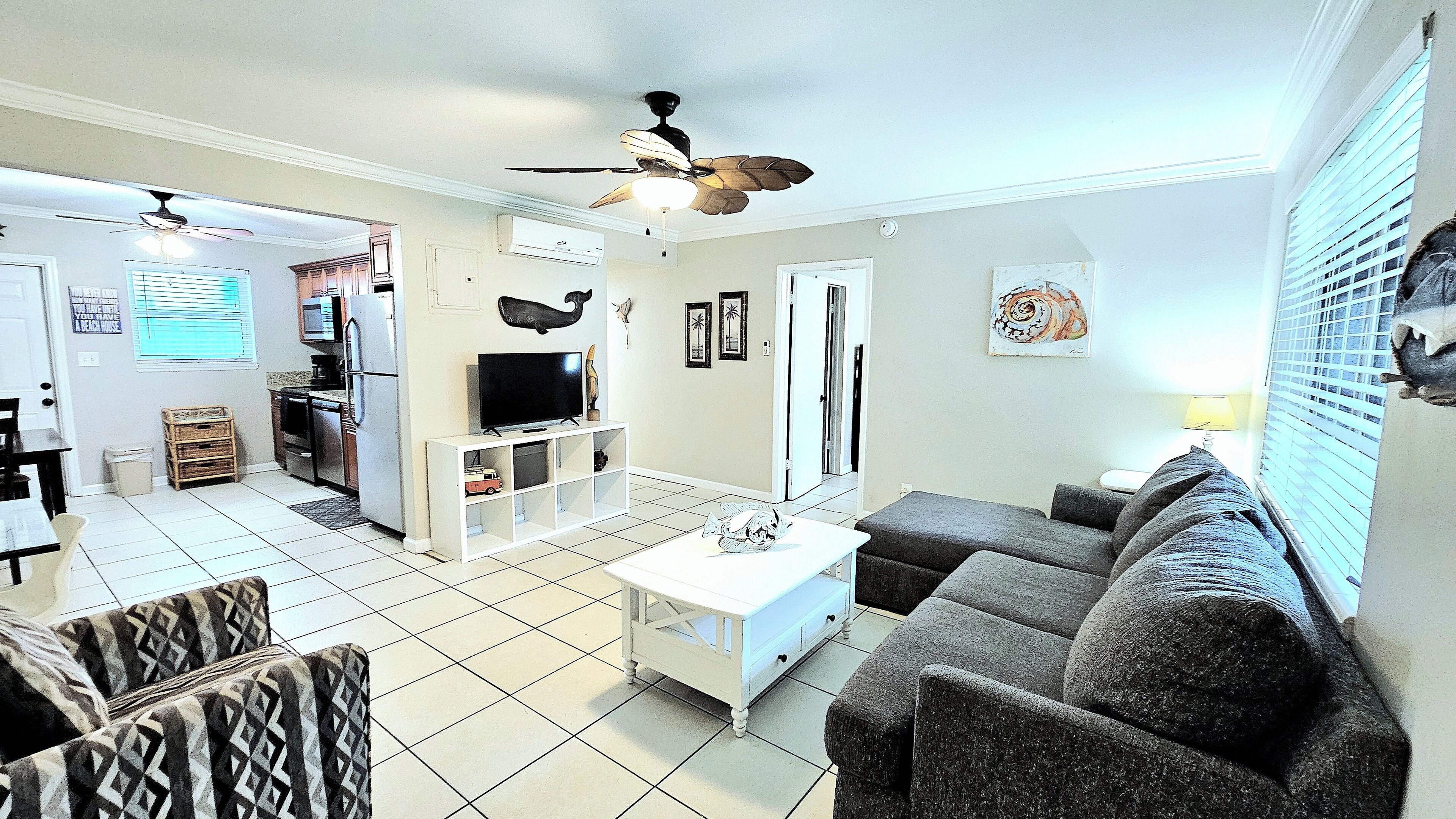 Un salon avec un canapé, une table basse, un téléviseur et un ventilateur de plafond.