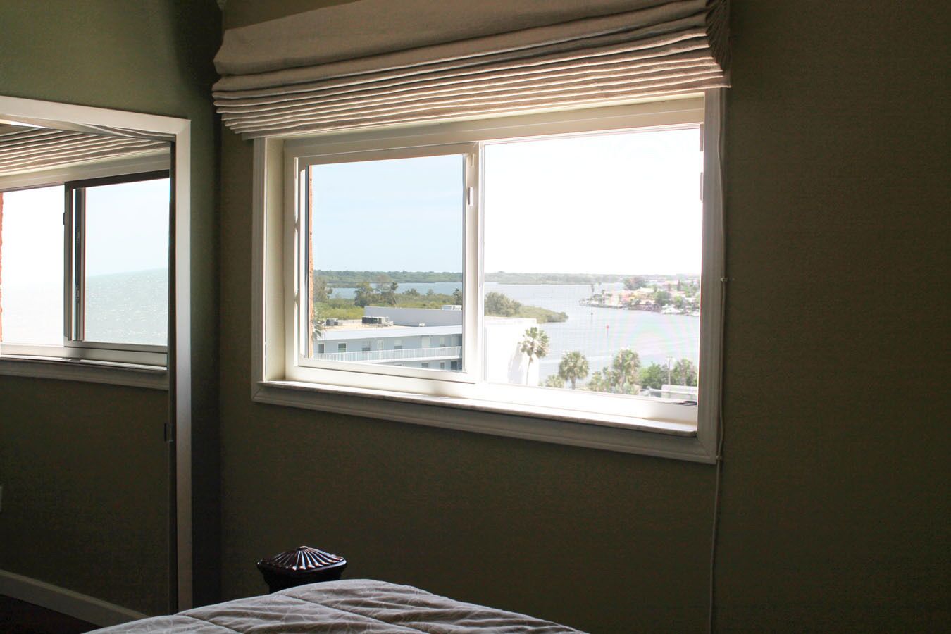 A bedroom with a large window offering a view of a body of water and distant buildings.
