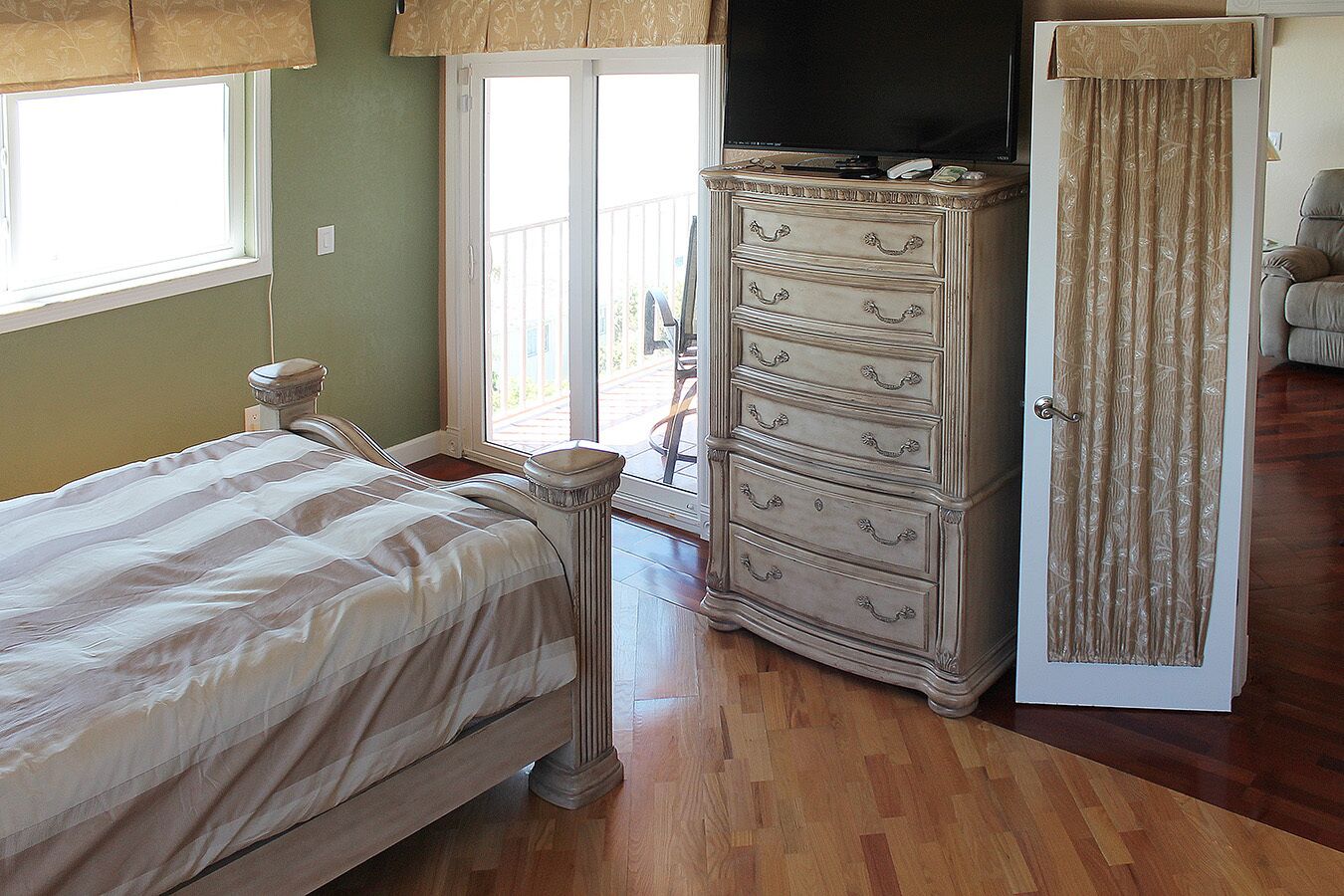 A bedroom with a bed, a dresser, a television, and a door with curtains.