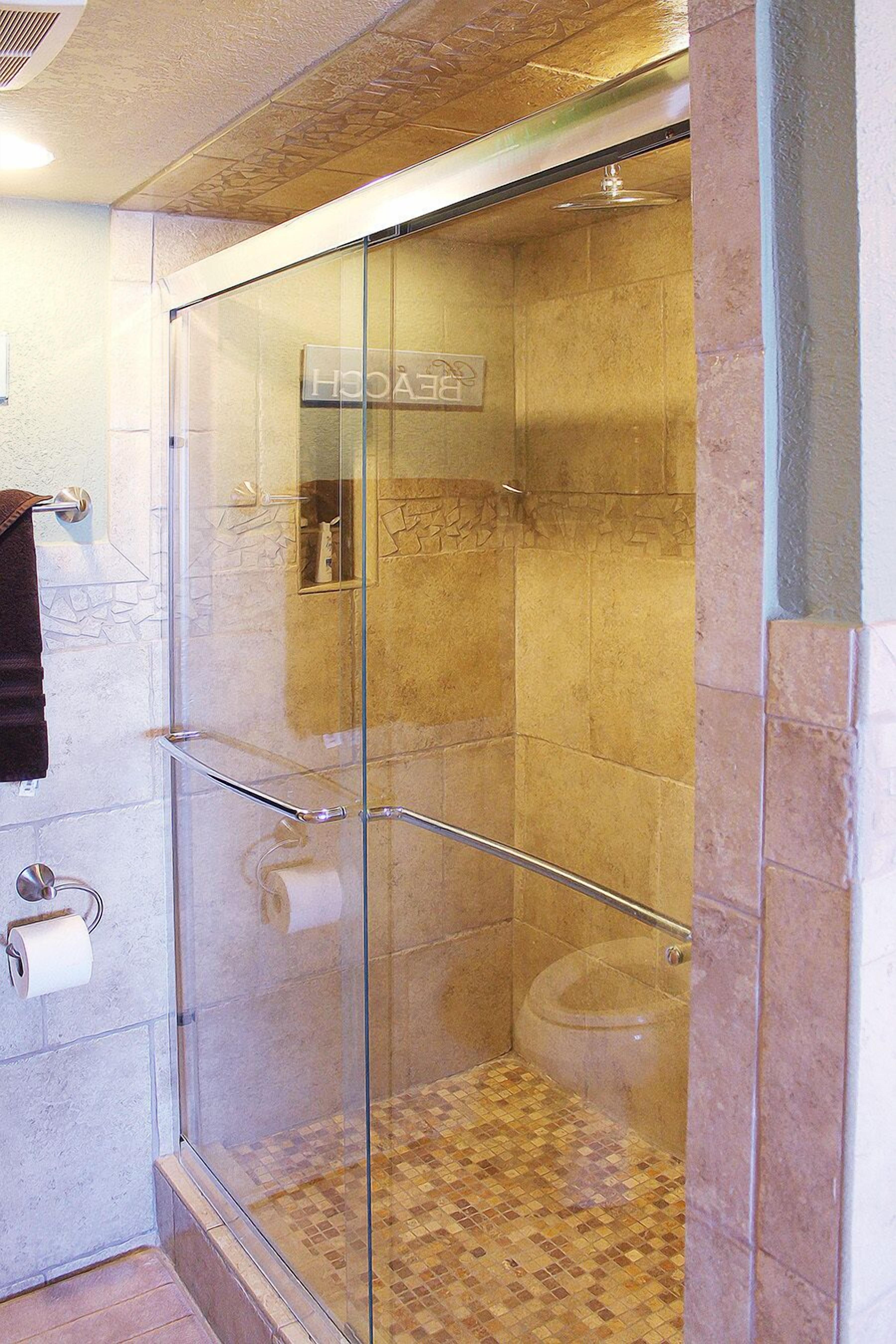 Een douchecabine met glazen wanden, een handdoekrek, toilet en een klein plankje met toiletartikelen.