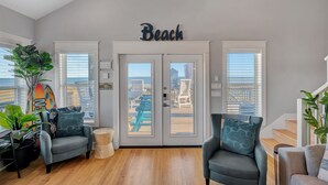 Un salon moderne avec une grande fenêtre, une enseigne «Plage» au-dessus de la porte et une vue sur le paysage urbain.