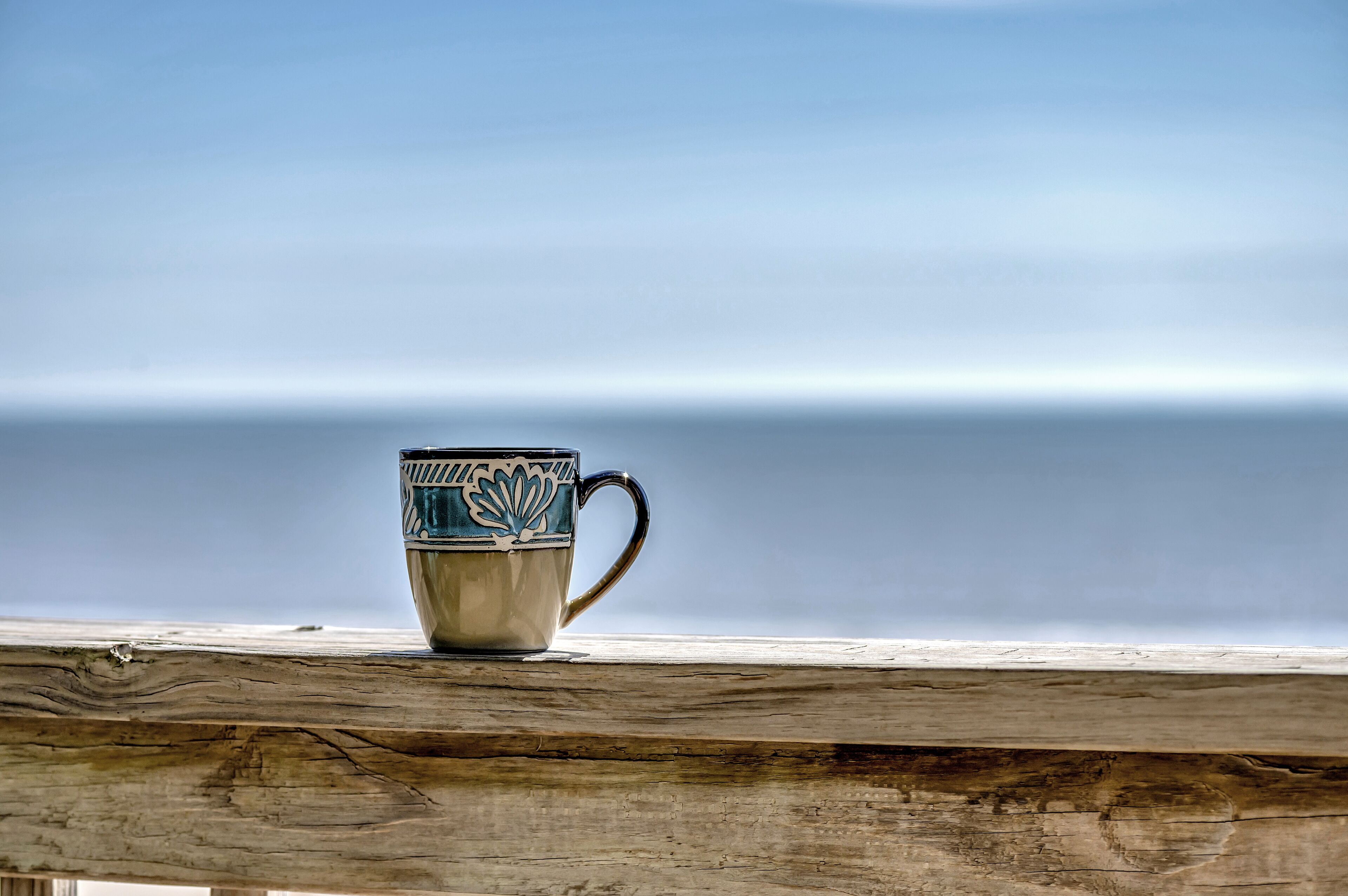 Une tasse posée sur une étagère en bois, avec vue sur l’océan.