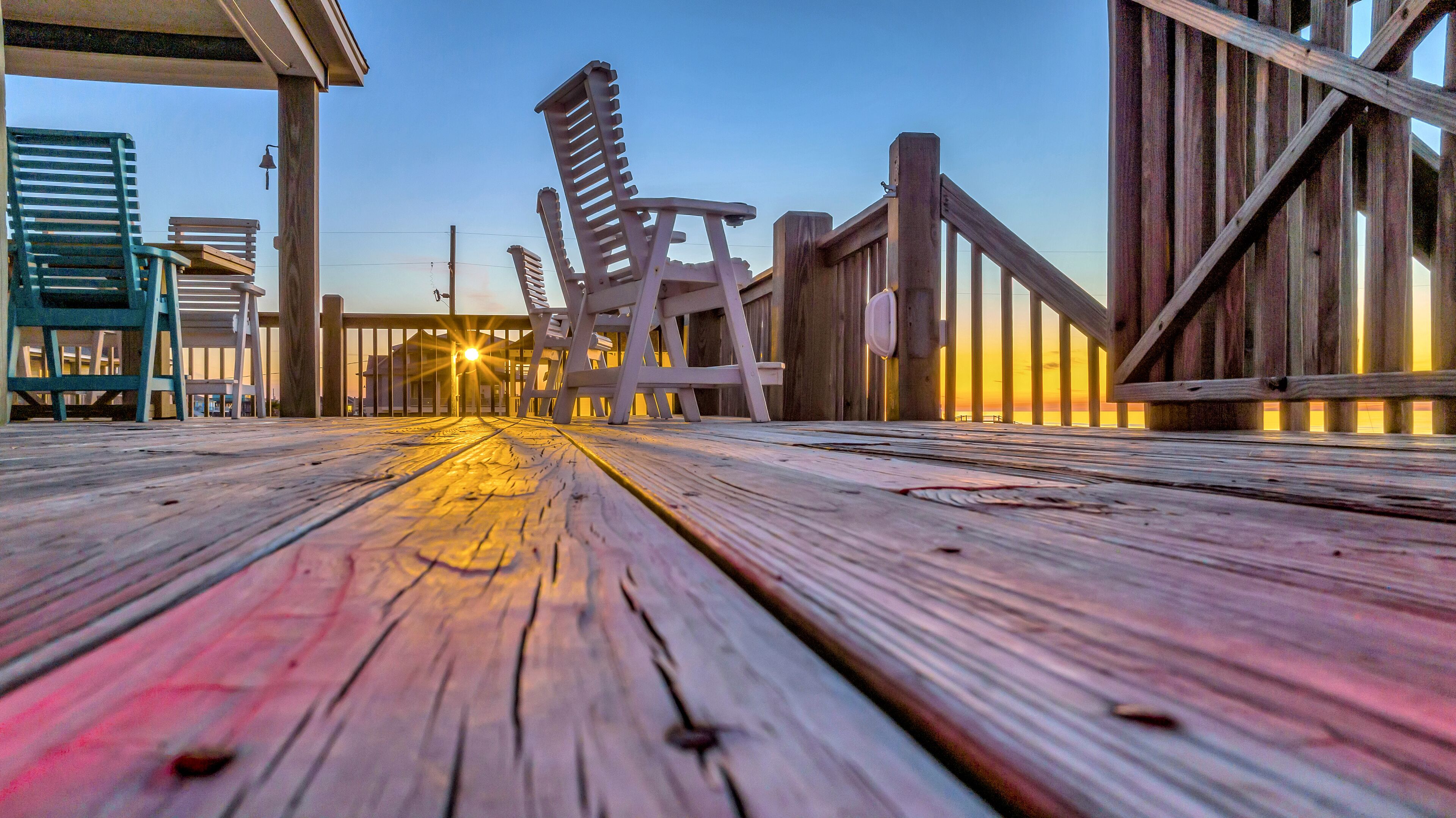A wooden deck with chairs and a view of the sunset.