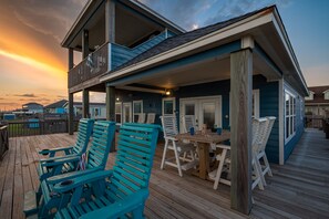 Une maison située sur la côte, dotée d’une terrasse en bois, d’un espace salon extérieur et d’un balcon offrant une vue sur la mer.