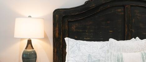 Ein Schlafzimmer mit einem hölzernen Kopfende, einem Nachttisch mit Lampe und zwei gerahmten Pflanzenbildern an der Wand.