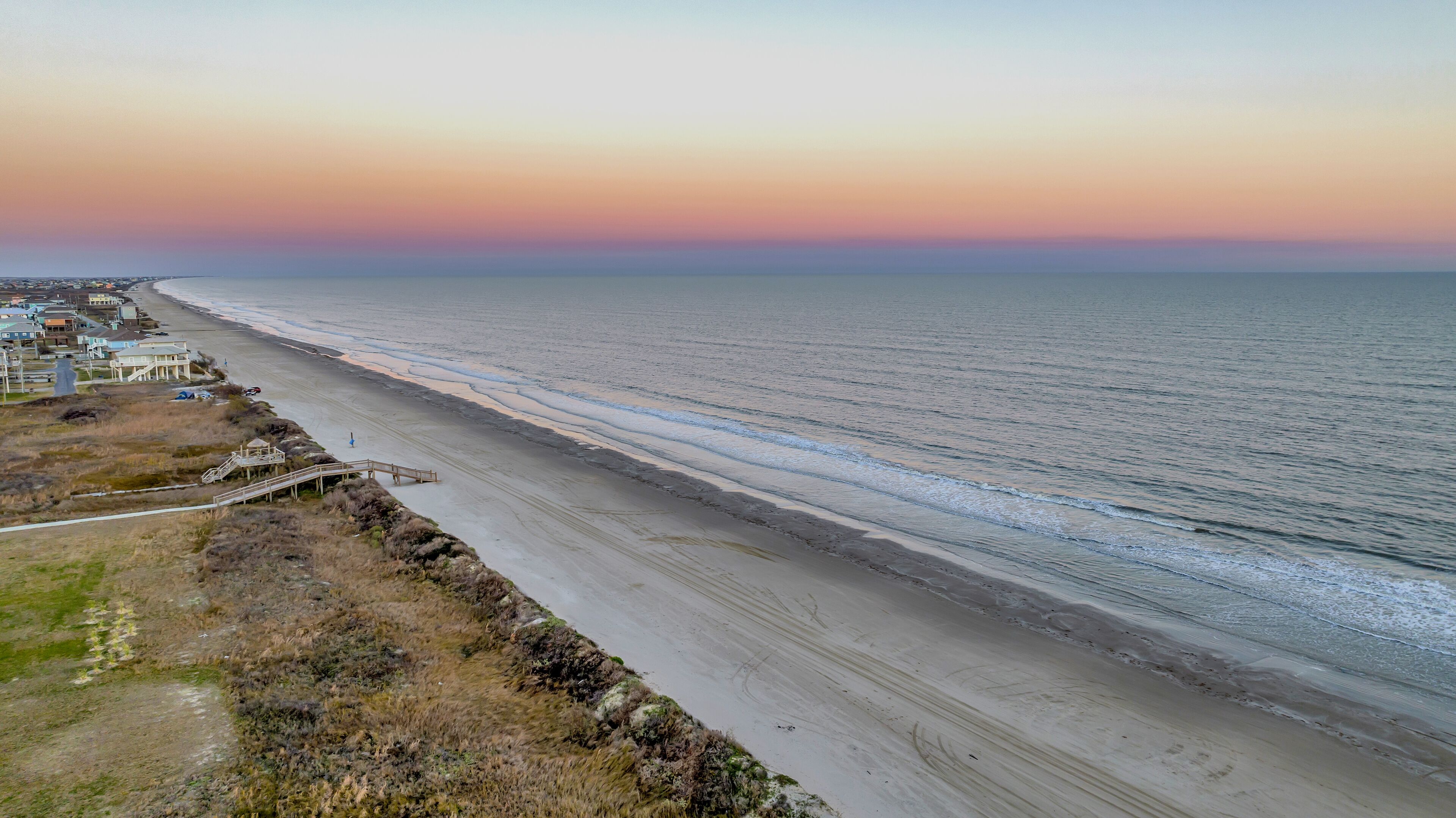Une vue côtière avec une plage, une promenade en bois et des bâtiments le long du rivage.