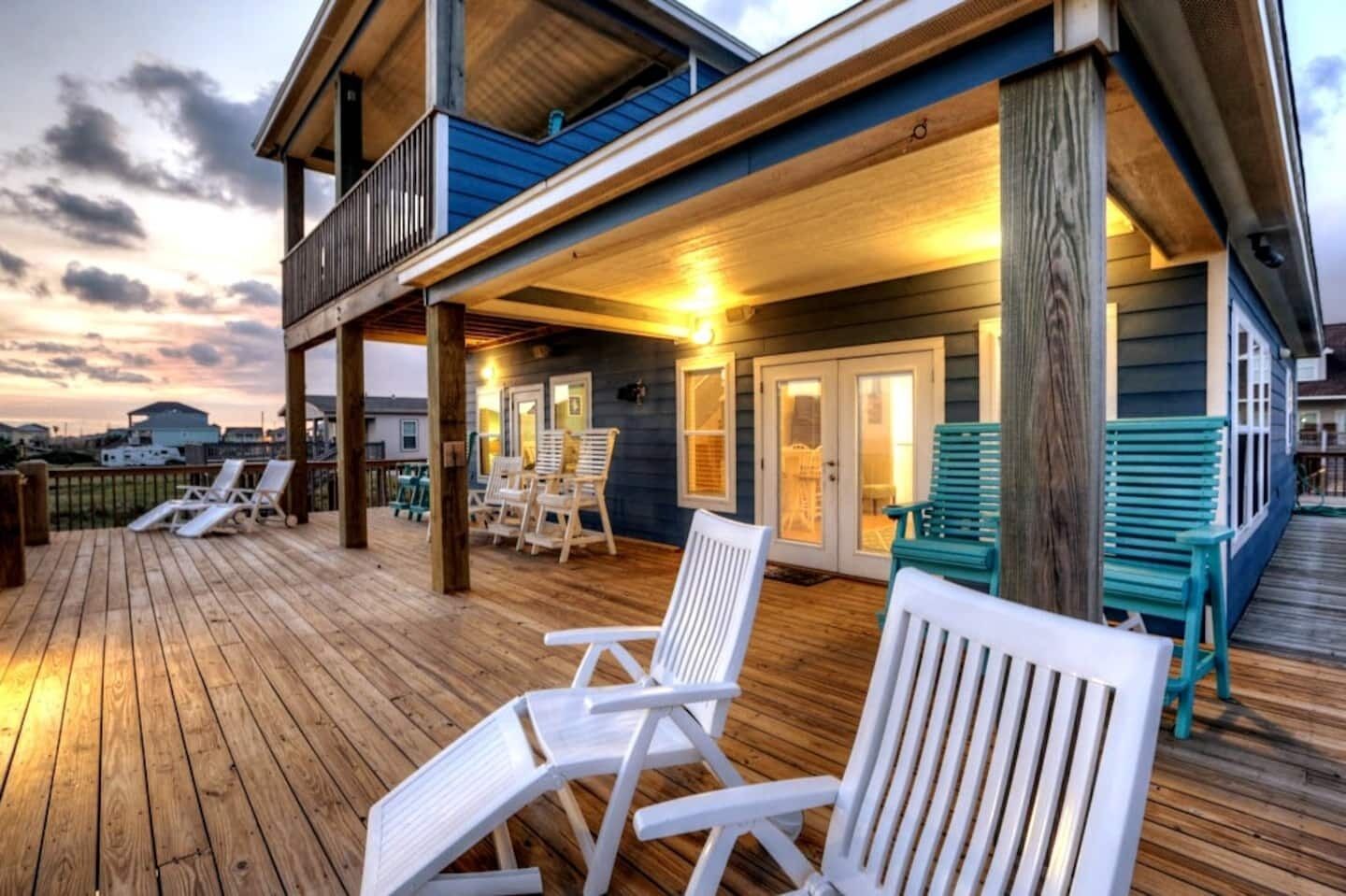 A wooden deck with white lounge chairs and a covered area with doors and windows.