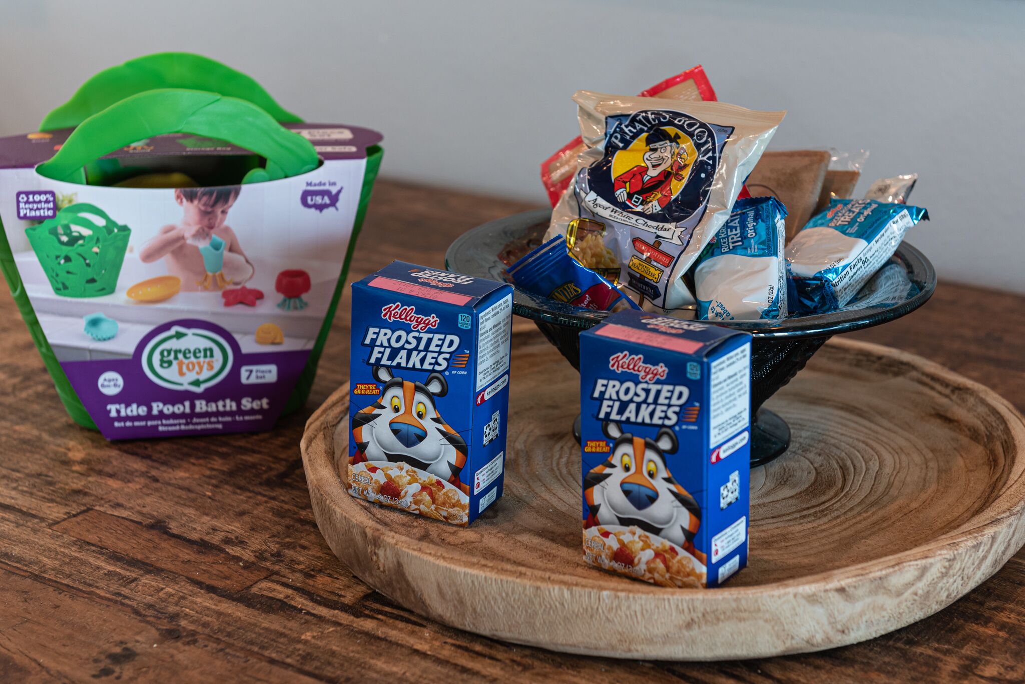 Une table en bois, un sac en tissu vert, deux boîtes de céréales Kellogg’s Frosted Flakes et un sac en plastique rempli de collations.