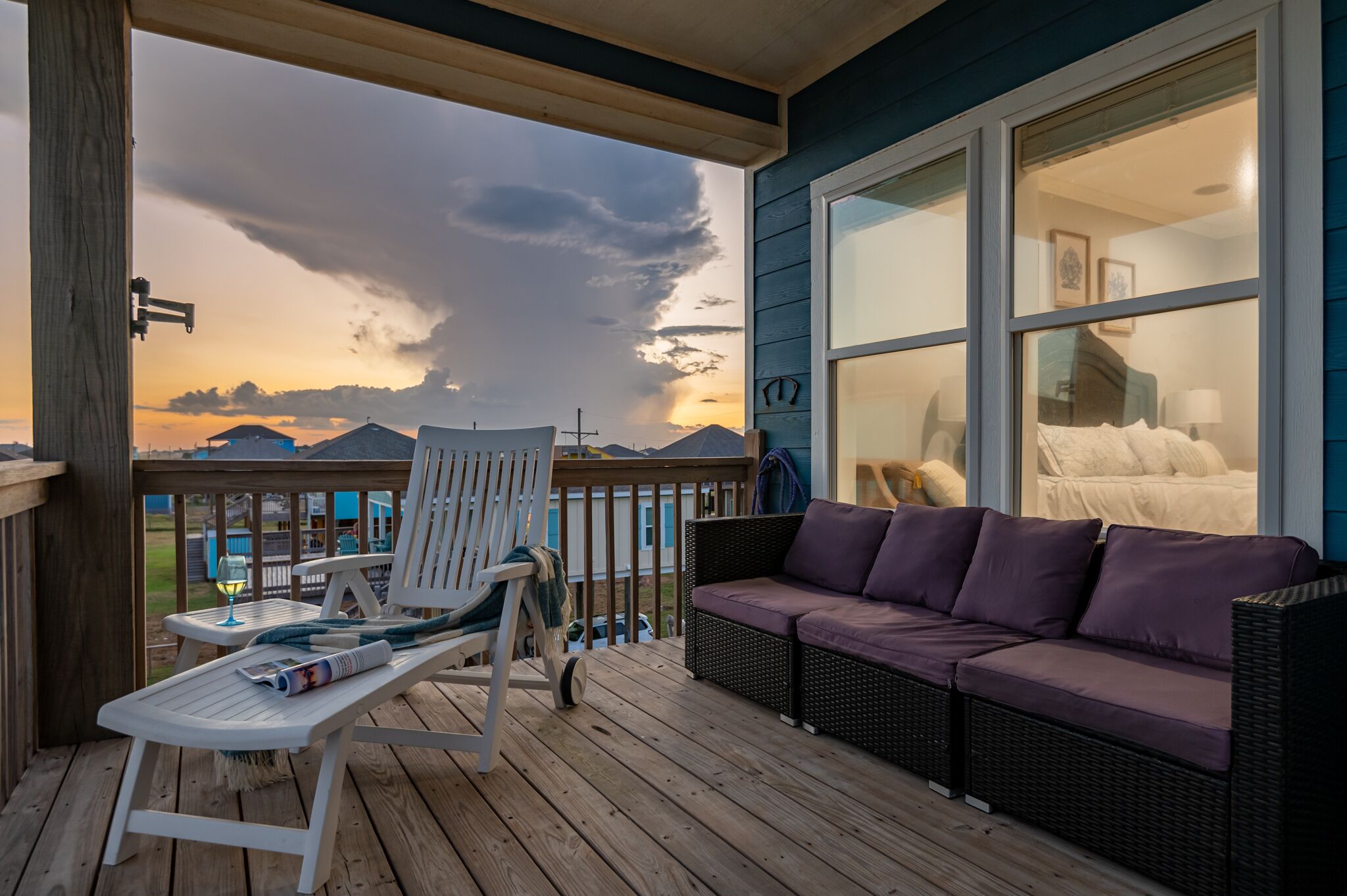 Een houten terras met een witte stoel en een paarse bank, met uitzicht op een berg en een zonsondergang.