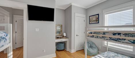 Habitación infantil con literas, televisor, escritorio y ventana con persianas.