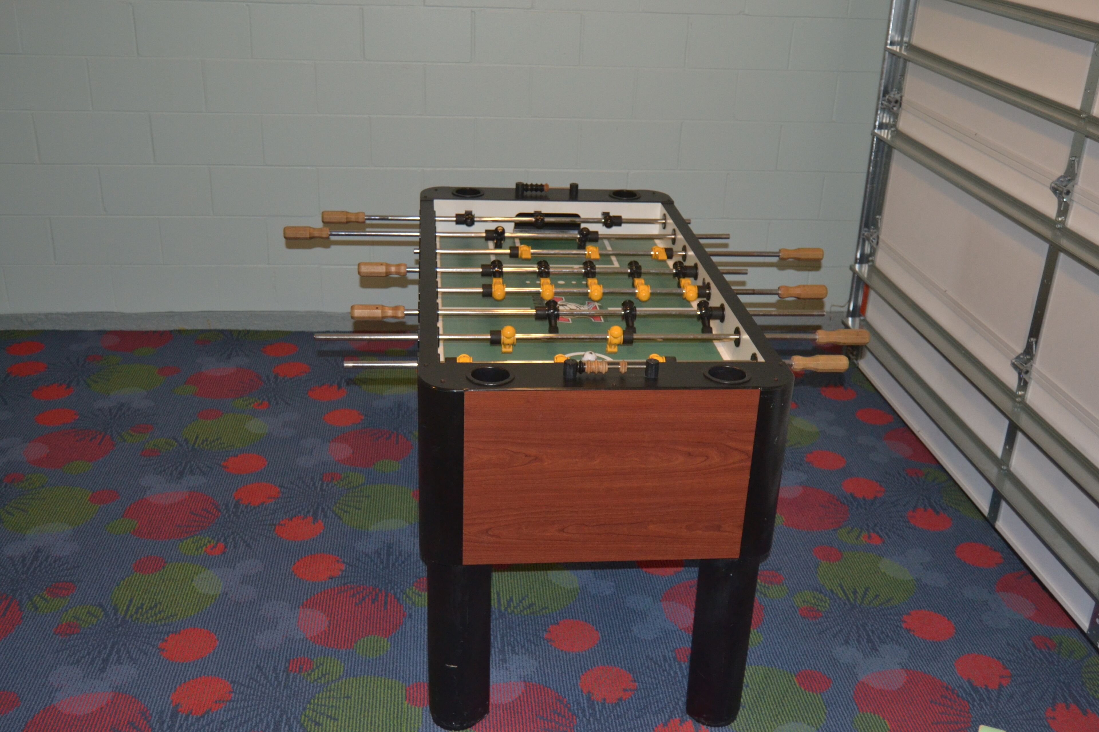 Une table de baby-foot dans une pièce dotée d’un tapis à motifs et d’un mur en briques blanches.