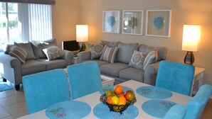 A living room with a grey sofa, blue chairs, a coffee table with a fruit bowl, and two wall-mounted lamps. - Orlando Villa near Disney, free Private Heated Pool, free Grill and free WiFi (Davenport)