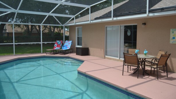 A covered outdoor swimming pool with lounge chairs and a table, surrounded by a building with a glass door. - Orlando Villa near Disney, free Private Heated Pool, free Grill and free WiFi (Davenport)
