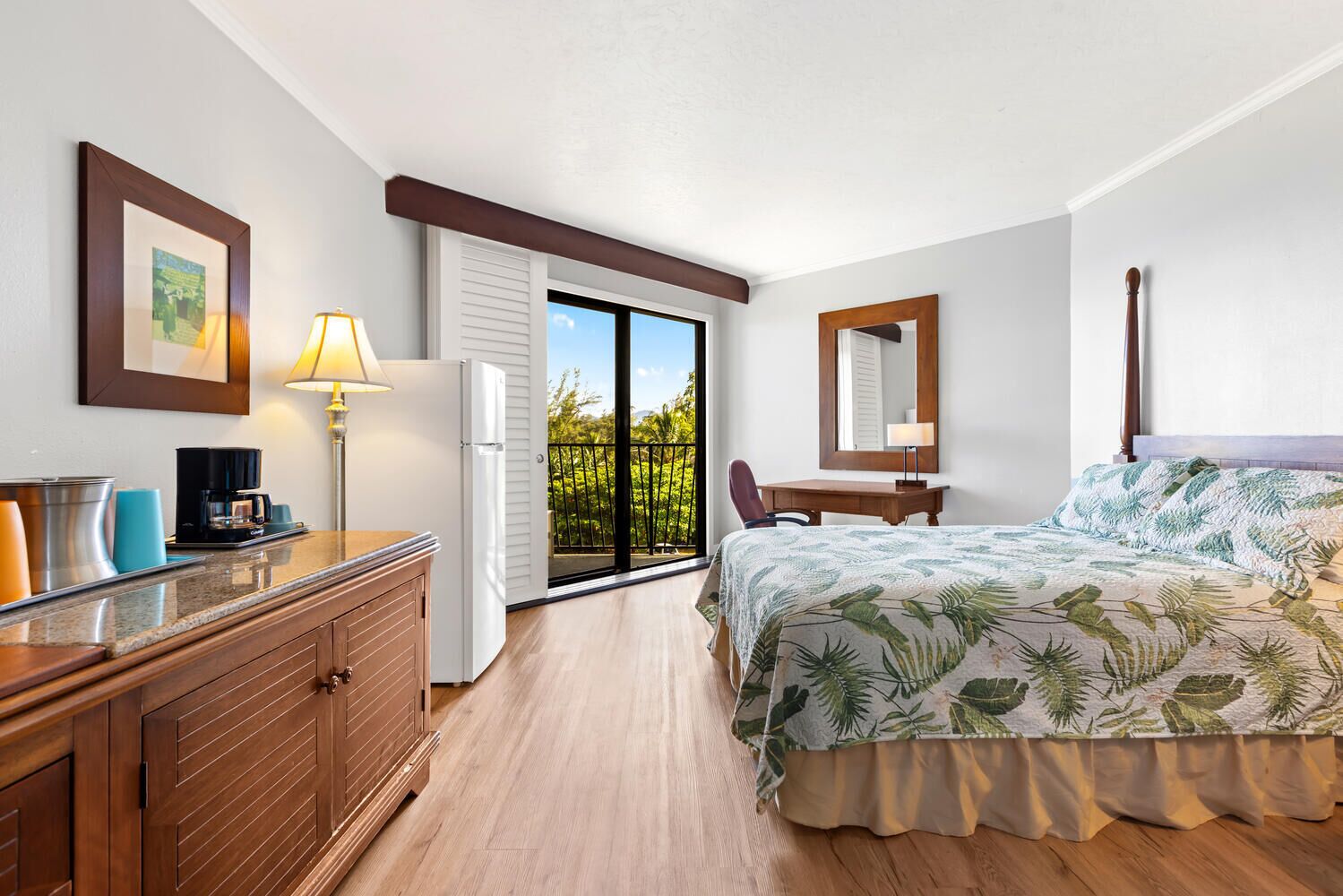 Ein Hotelzimmer mit Bett, Schreibtisch, Stuhl, Kühlschrank, Kaffeemaschine und einem Fenster mit Blick auf Grünflächen.