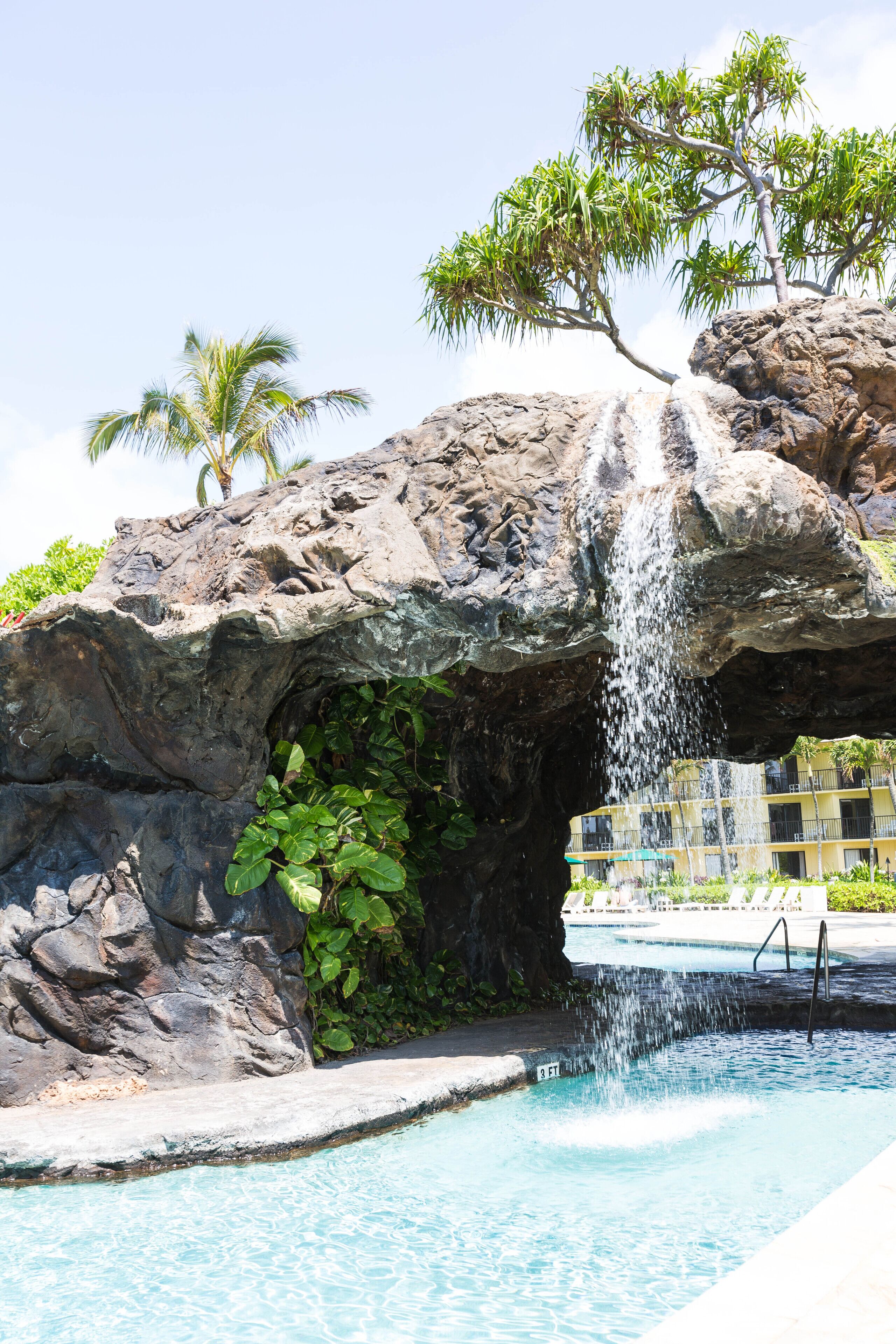 A pool with a waterfall feature, surrounded by rocks and greenery.