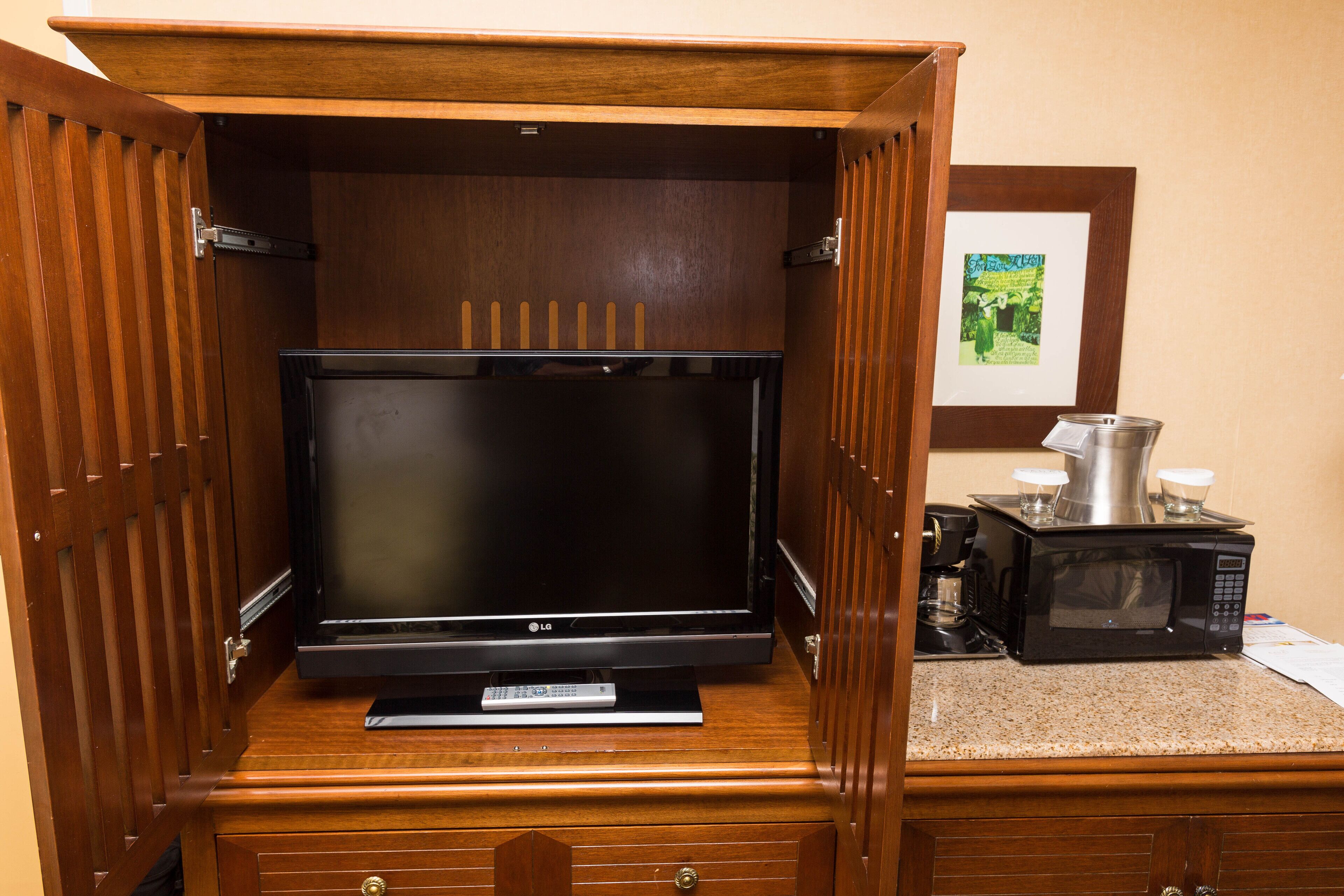 A wooden cabinet with a flat-screen TV and a microwave on top.
