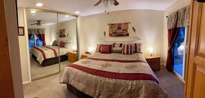 A bedroom with a large bed, two bedside tables, a ceiling fan, a mirror, and a window with curtains.