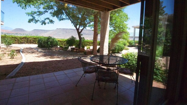 An outdoor patio with a table and chairs, surrounded by trees and a view of distant hills.