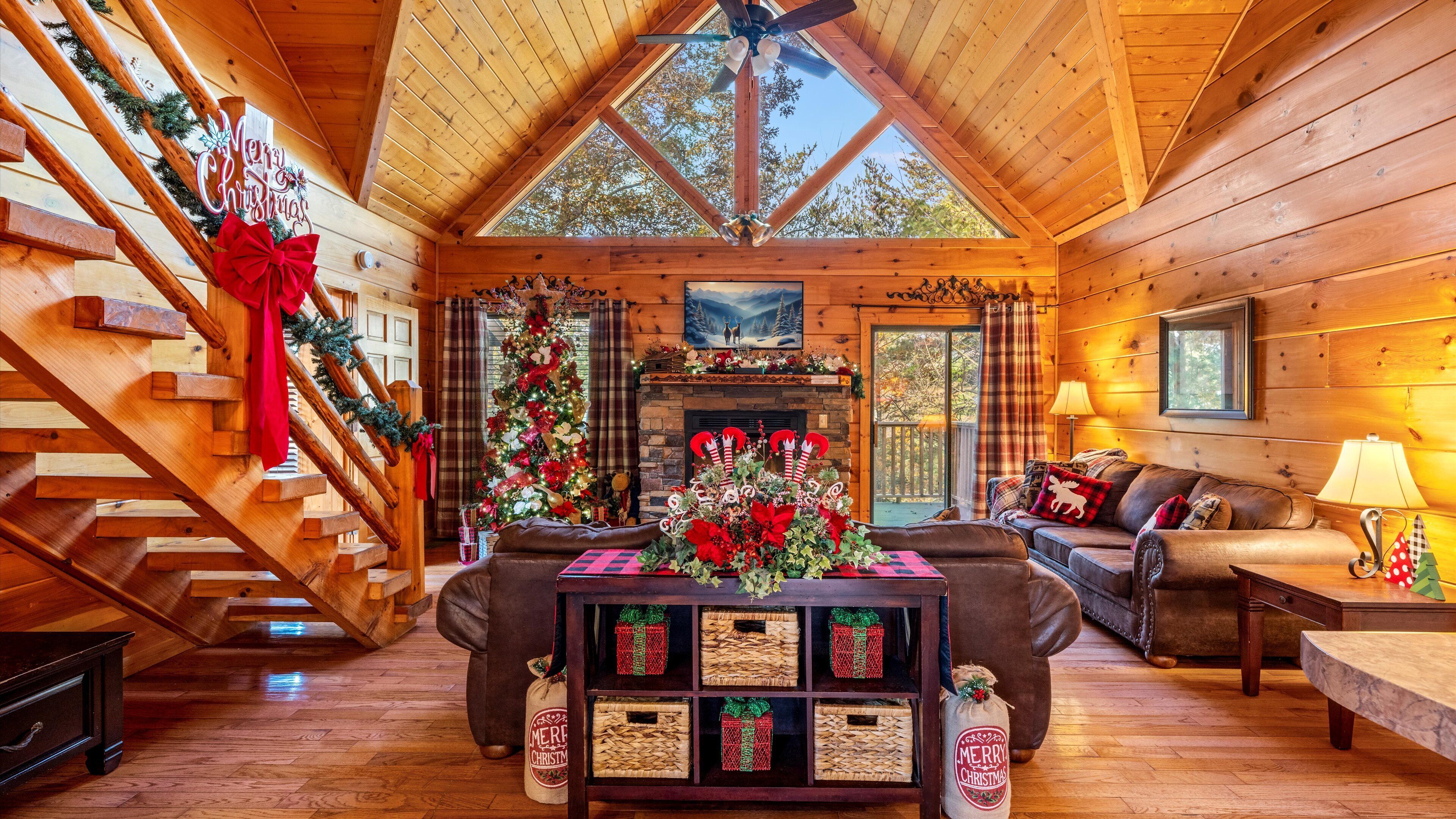 A cozy log cabin interior with a fireplace, a Christmas tree, and a staircase with garlands.