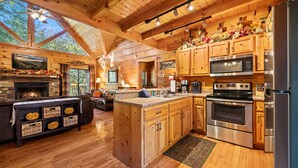 Eine gemütliche Landhausküche mit Holzschränken, einem Kamin aus Stein und einer großen Kochinsel mit Spüle.
