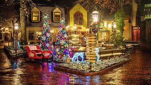 Ein festlich dekorierter Außenbereich mit Weihnachtsbäumen, einem Brunnen und einer Sitzgelegenheit mit Coca-Cola-Branding.