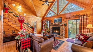 Ein gemütliches Blockhaus-Interieur mit Kamin, Weihnachtsbaum und einer mit festlicher Dekoration geschmückten Treppe.