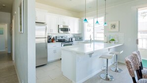 Une cuisine moderne avec des meubles blancs, des appareils en acier inoxydable et un îlot central doté de tabourets de bar.