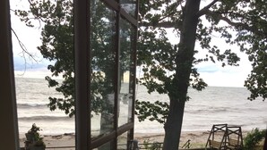 A view through a glass door of a grassy yard with a swing set and a bench, overlooking a beach with waves. - Beachfront Historic home 2br/1Ba apt. w/  Steam Shower, WiFi, Netflix, Disney+  (Dunkirk)