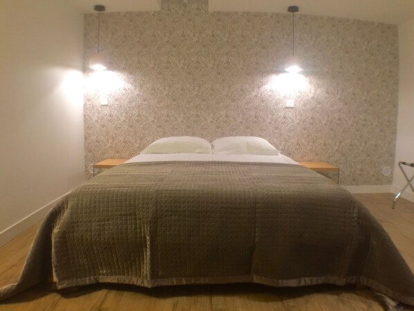 A neatly made bed with a quilted blanket, two bedside tables, and a patterned wallpaper.