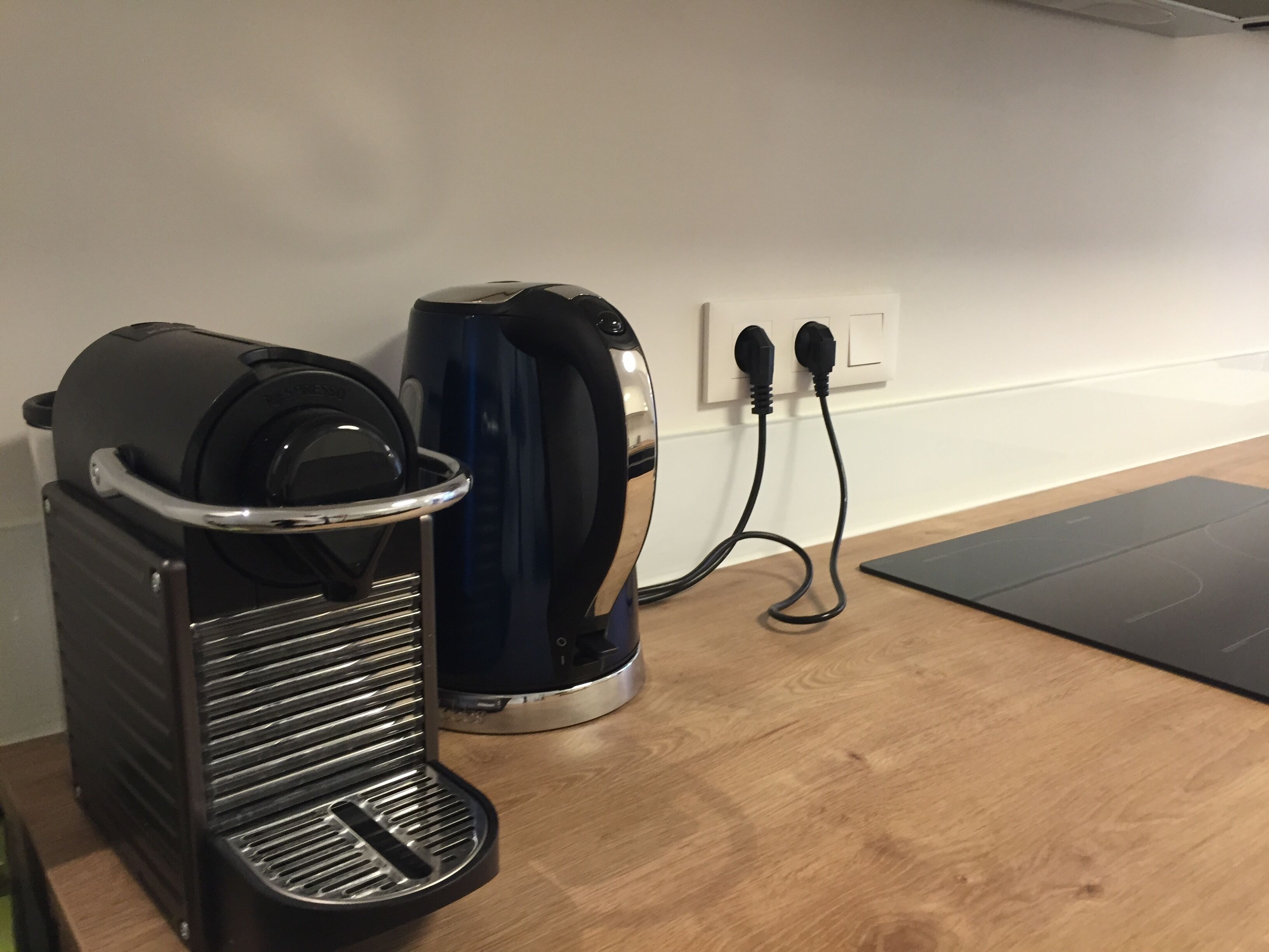 A coffee maker and a kettle on a wooden table, connected to a power outlet.