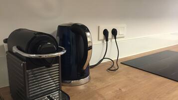 A coffee maker and a kettle on a wooden table, connected to a power outlet.