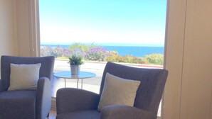 A room with two grey armchairs, a small round table, and a view of the sea.