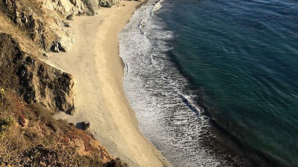 A coastal landscape with a sandy beach, rocky cliffs, and calm ocean waters.