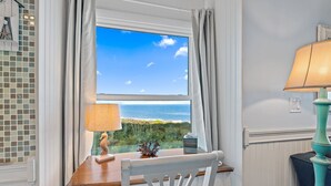 Une pièce avec vue sur l’océan, visible par une fenêtre, un bureau en bois avec une lampe et une chaise.