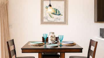 Un comedor con mesa de madera, cuatro sillas, una obra de arte enmarcada de una tortuga y una lámpara colgante.