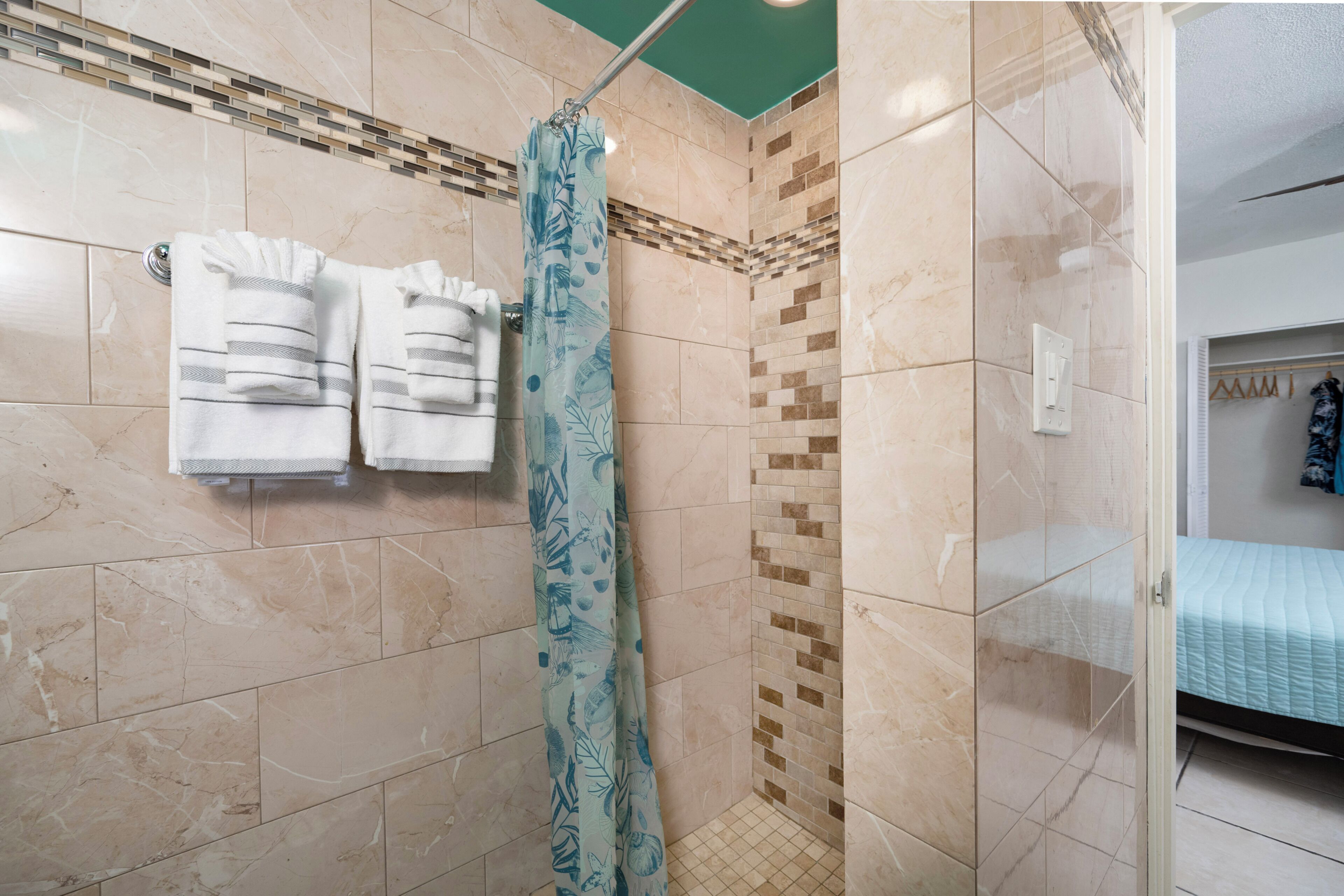 A bathroom with a shower, tiled walls, and a bed in the adjacent room.