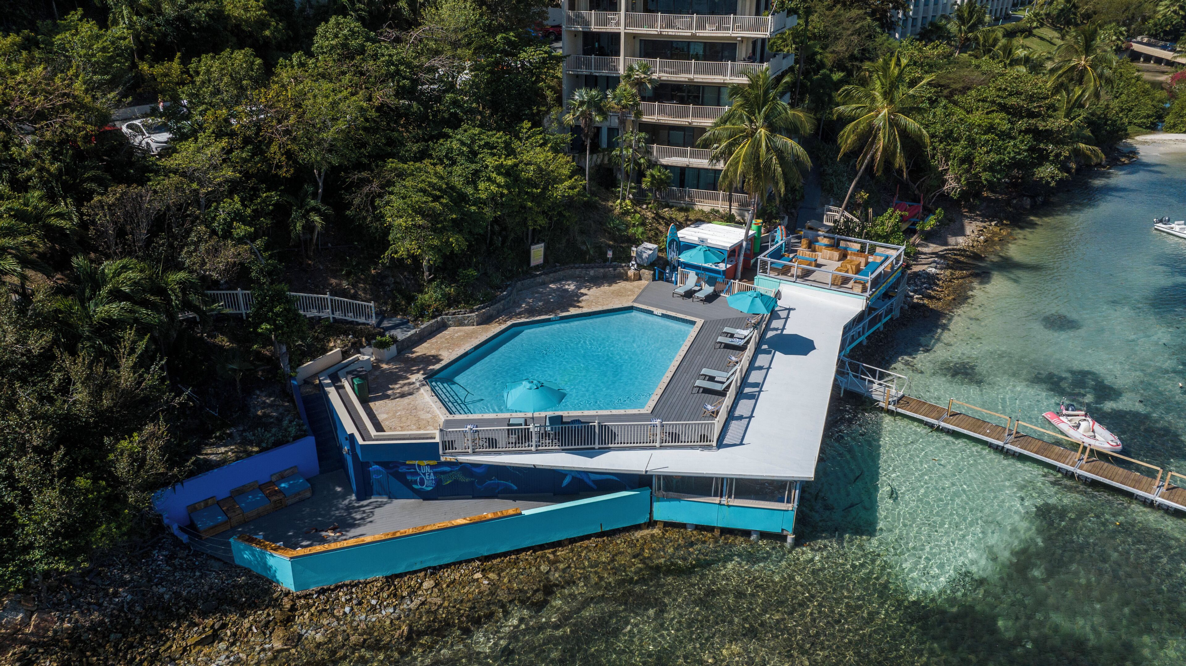 Vista aérea de un resort con una piscina grande, un muelle y una playa.