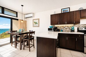 A modern kitchen with dark wood cabinets, a white countertop, and a dining area with a view of the ocean. - Updated: Luxury Villa, Amazing Views with Pool + Generator (Nazareth)